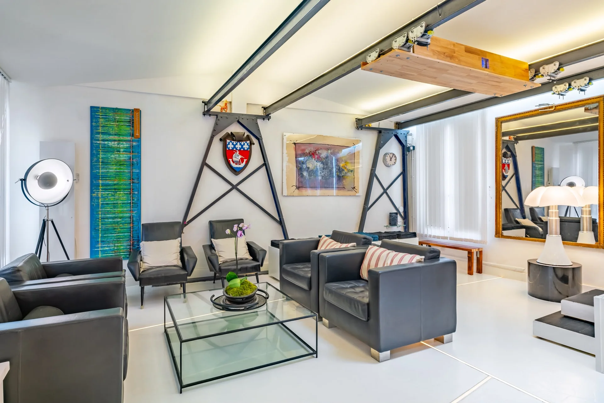 Salon du loft industriel à Reuilly-Diderot avec fauteuils en cuir, verrières et structure métallique apparente