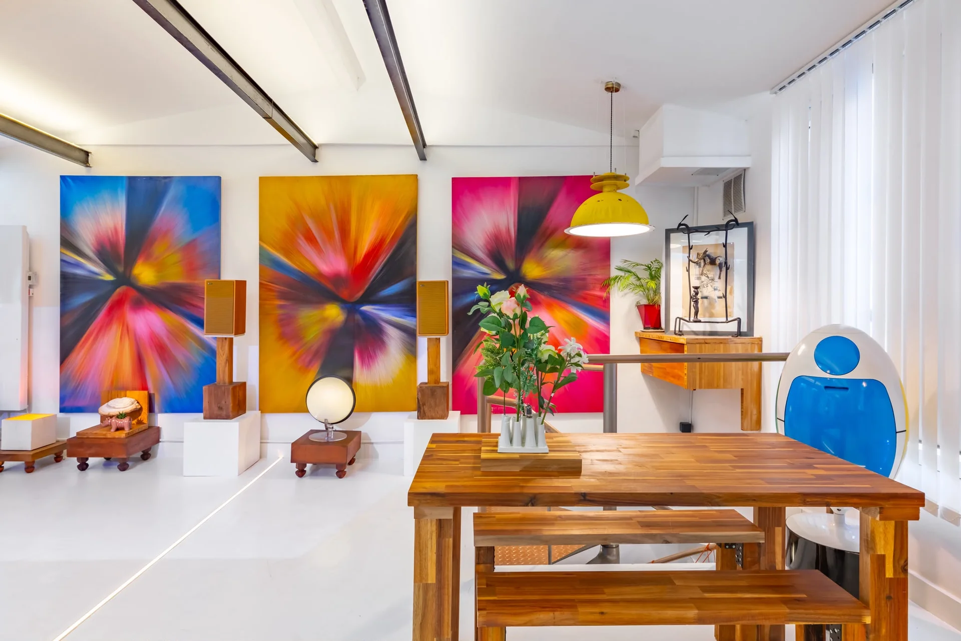 Espace repas et atelier du loft rétro-futuriste à Paris avec grande table en bois et triptyque coloré