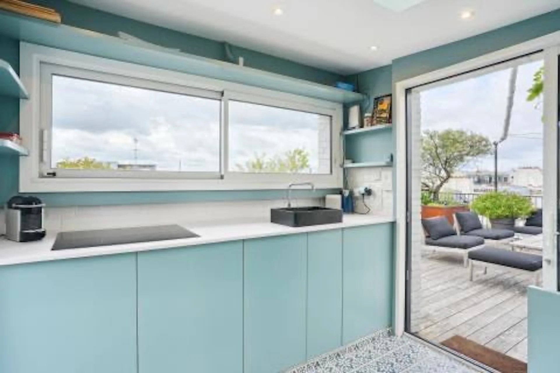 Espace de réception turquoise avec baies vitrées ouvertes sur terrasse panoramique et vue urbaine parisienne