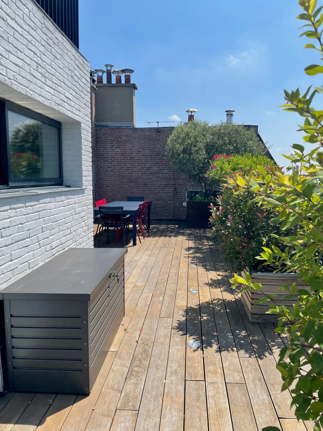 Terrasse rooftop avec terrasse en bois, mobilier rouge, briques blanches et noires, végétation, vue dégagée sur Paris
