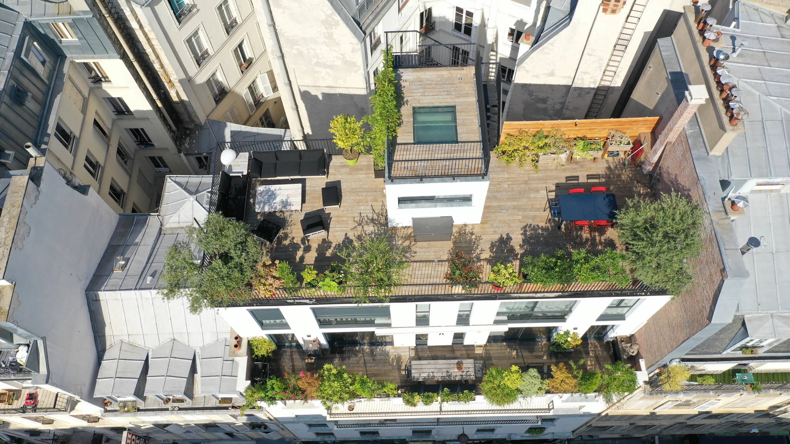 Rooftop parisien avec terrasse bois, zones de verdure et mobilier lounge face aux toits de Montmartre