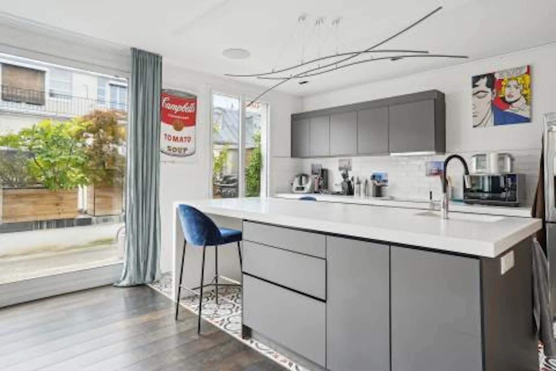 Cuisine moderne avec îlot central gris, mobilier minimaliste et baies vitrées ouvertes sur terrasse végétalisée