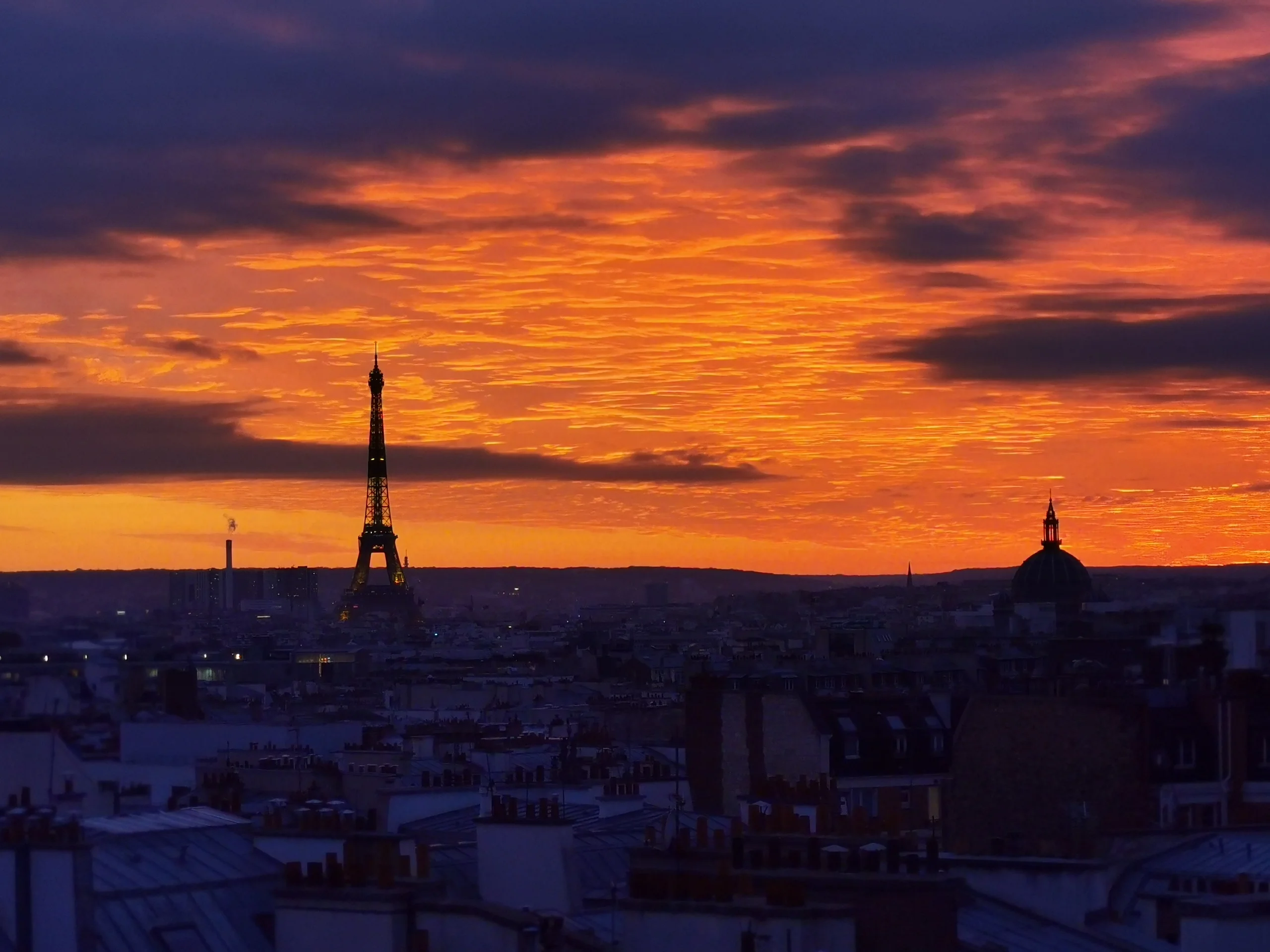 Panorama urbain parisien au coucher de soleil avec la Tour Eiffel illuminée et la basilique du Sacré-Cœur visibles à l'horizon