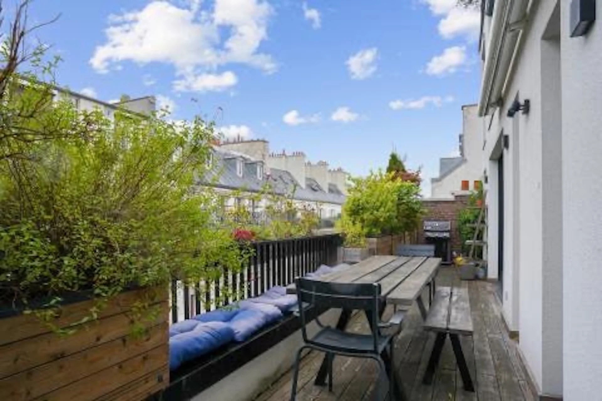 Terrasse rooftop avec mobilier gris, jardinières végétales et vue sur toits haussmanniens parisiens