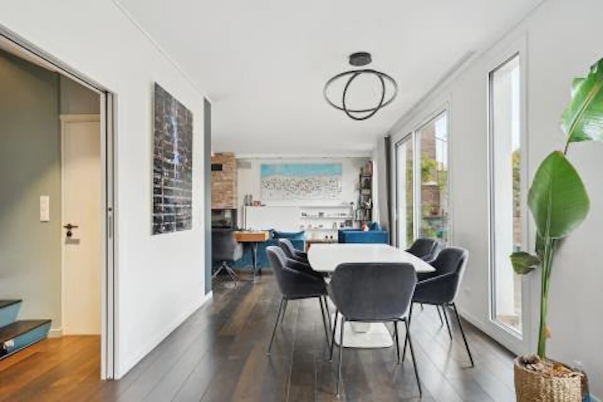 Espace lumineux avec parquet bois, table blanche, chaises noires et baies vitrées ouvrant sur Montmartre