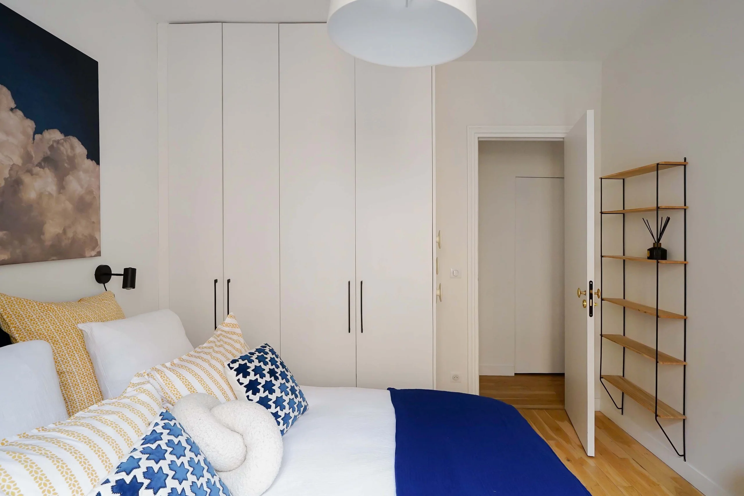 Chambre haussmannienne aux murs blancs, lit avec rangements intégrés, parquet clair et plafonnier suspendu