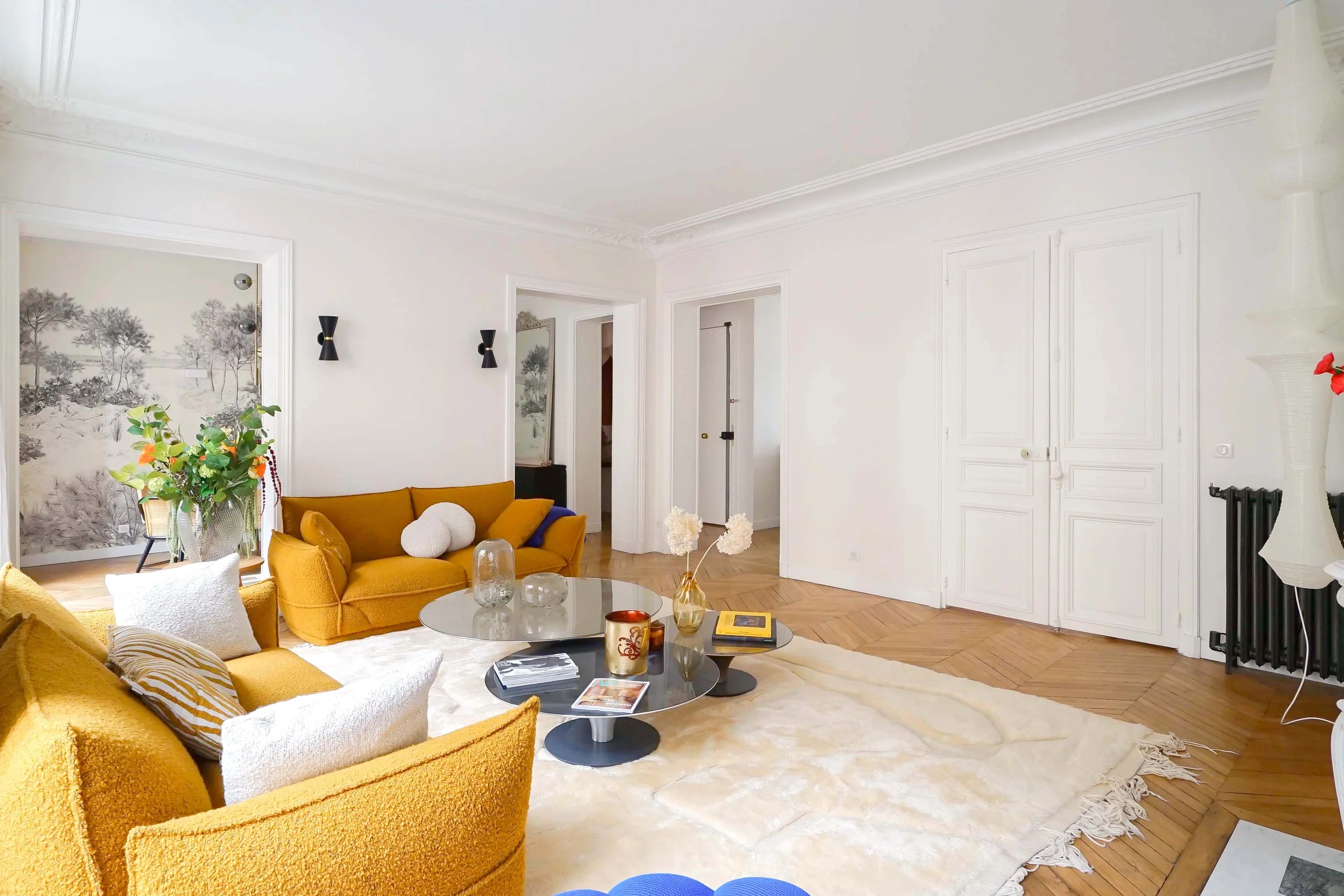 Salon haussmannien lumineux avec canapés jaune ocre, parquet clair, murs blanc cassé et portes blanches