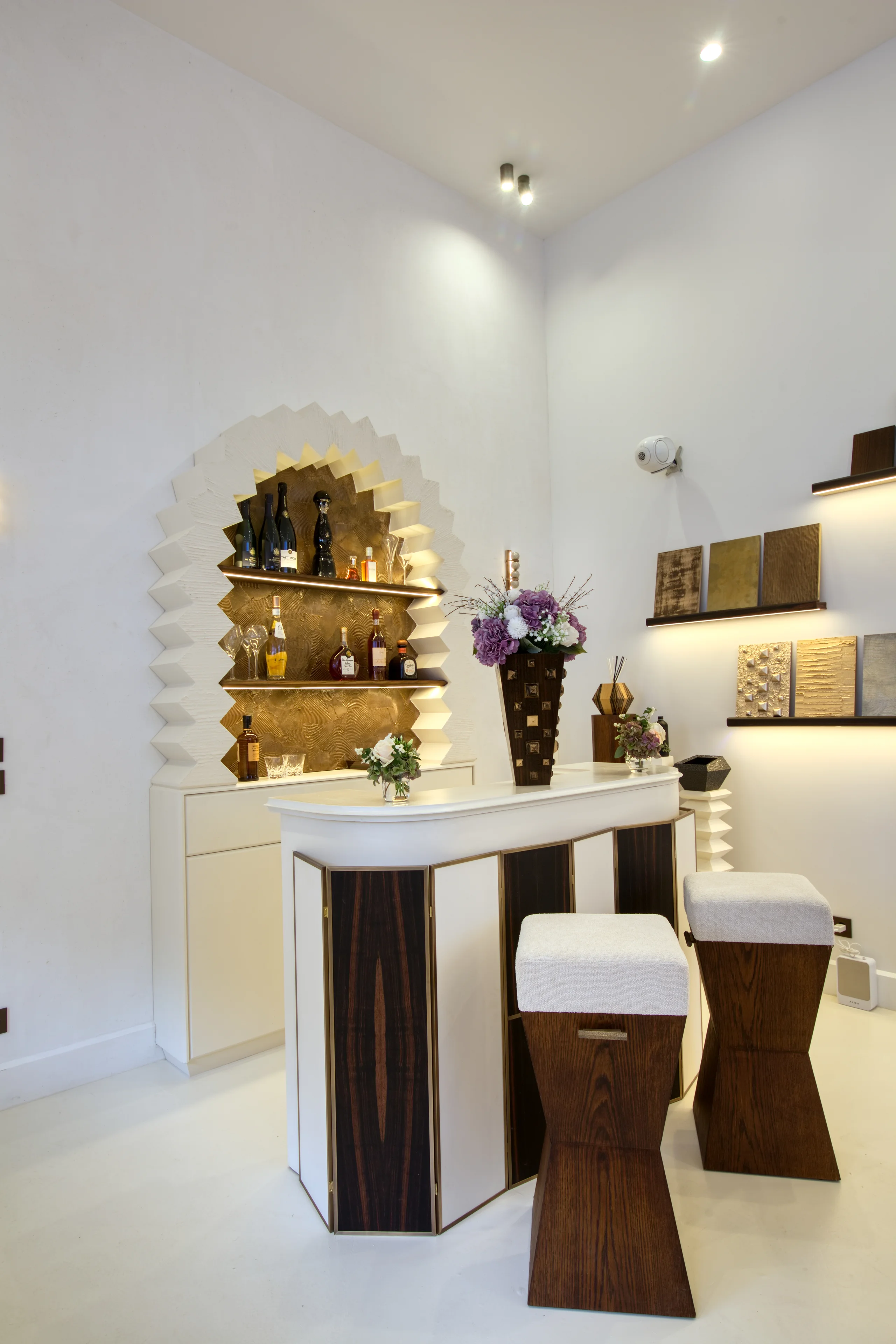 Grand Salon avec bar blanc et bois, comptoir éclairé, niche arrondie dorée, étagères murales illuminées, mobilier minimaliste