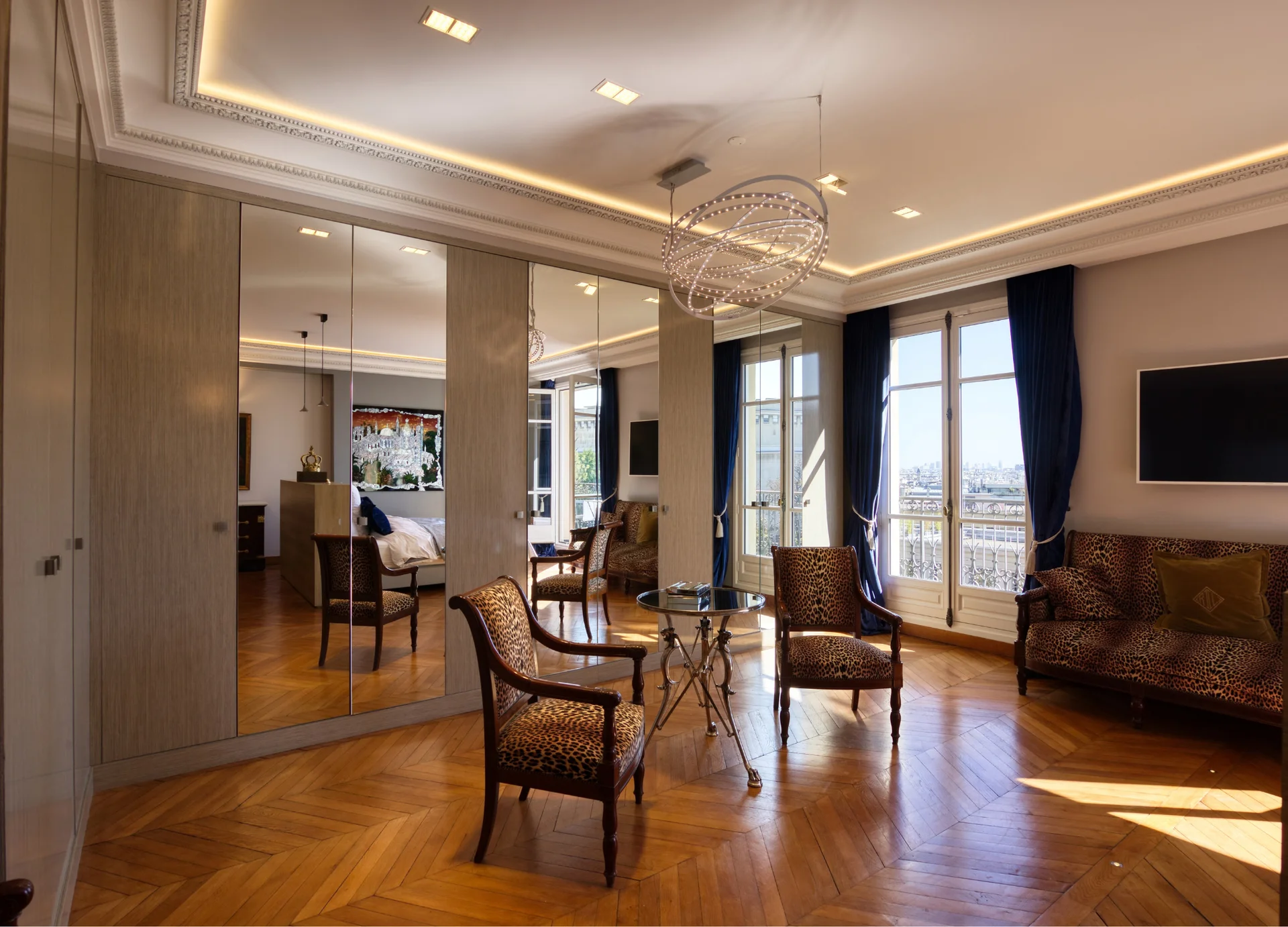 chambre élégante aux murs beige, parquet blond, lustre cristal, baies vitrées dominant Paris et la Tour Eiffel