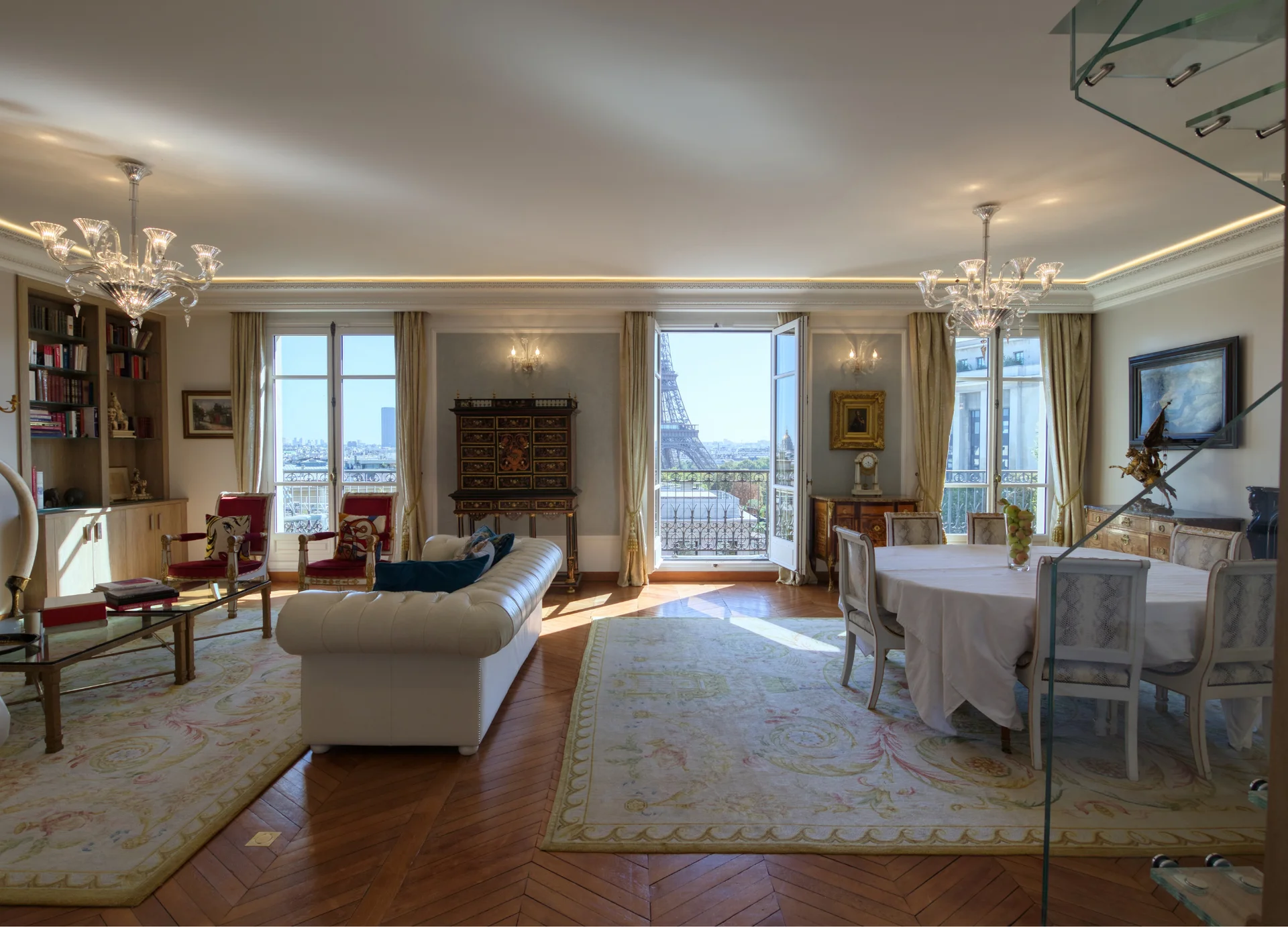 Salon spacieux aux murs crème, parquet bois, lustres cristal, baies vitrées ouvrant sur la Tour Eiffel