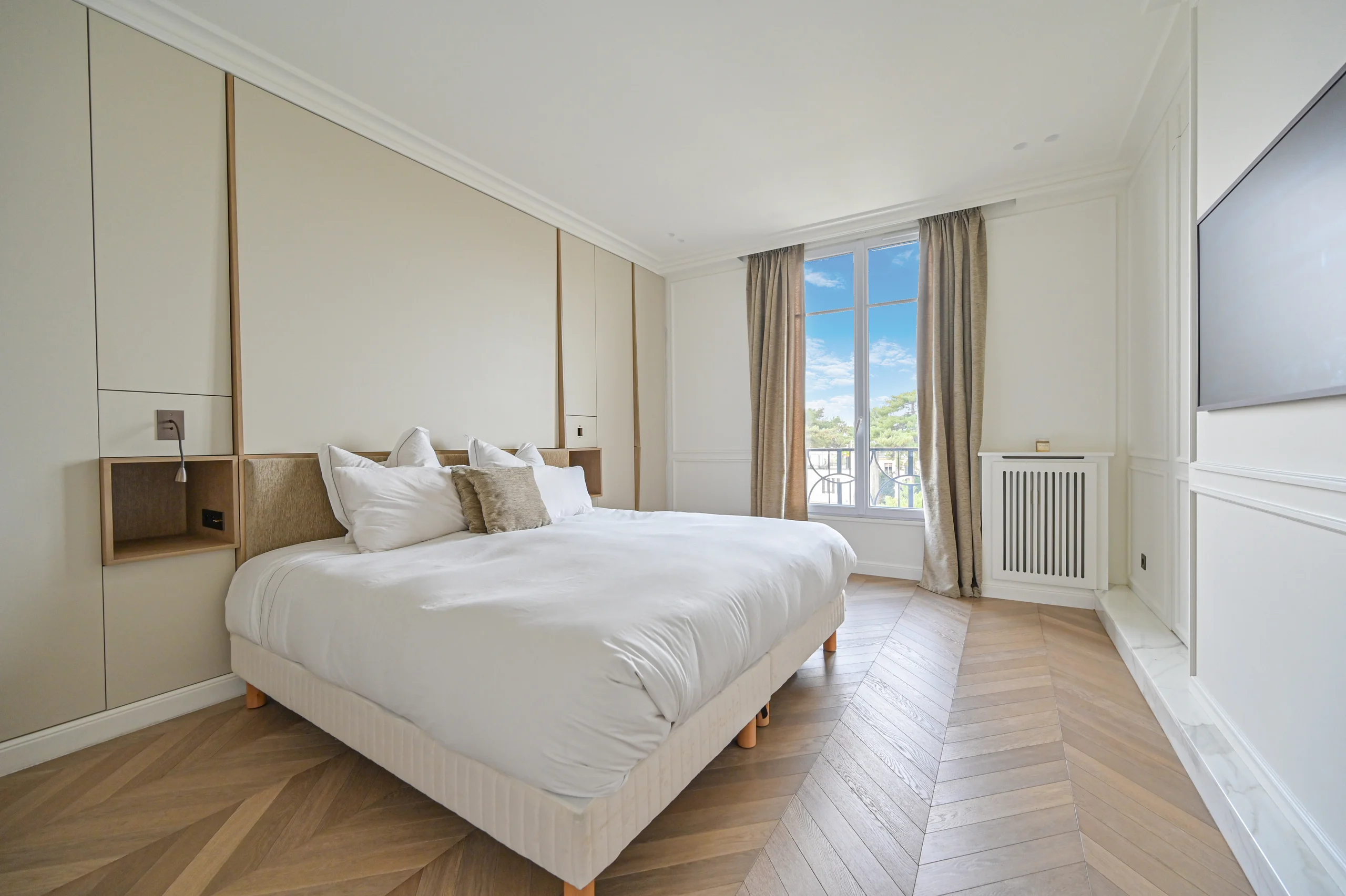 Chambre spacieuse aux murs crème, lit blanc, parquet clair, baies vitrées donnant sur terrasse avec vue parc