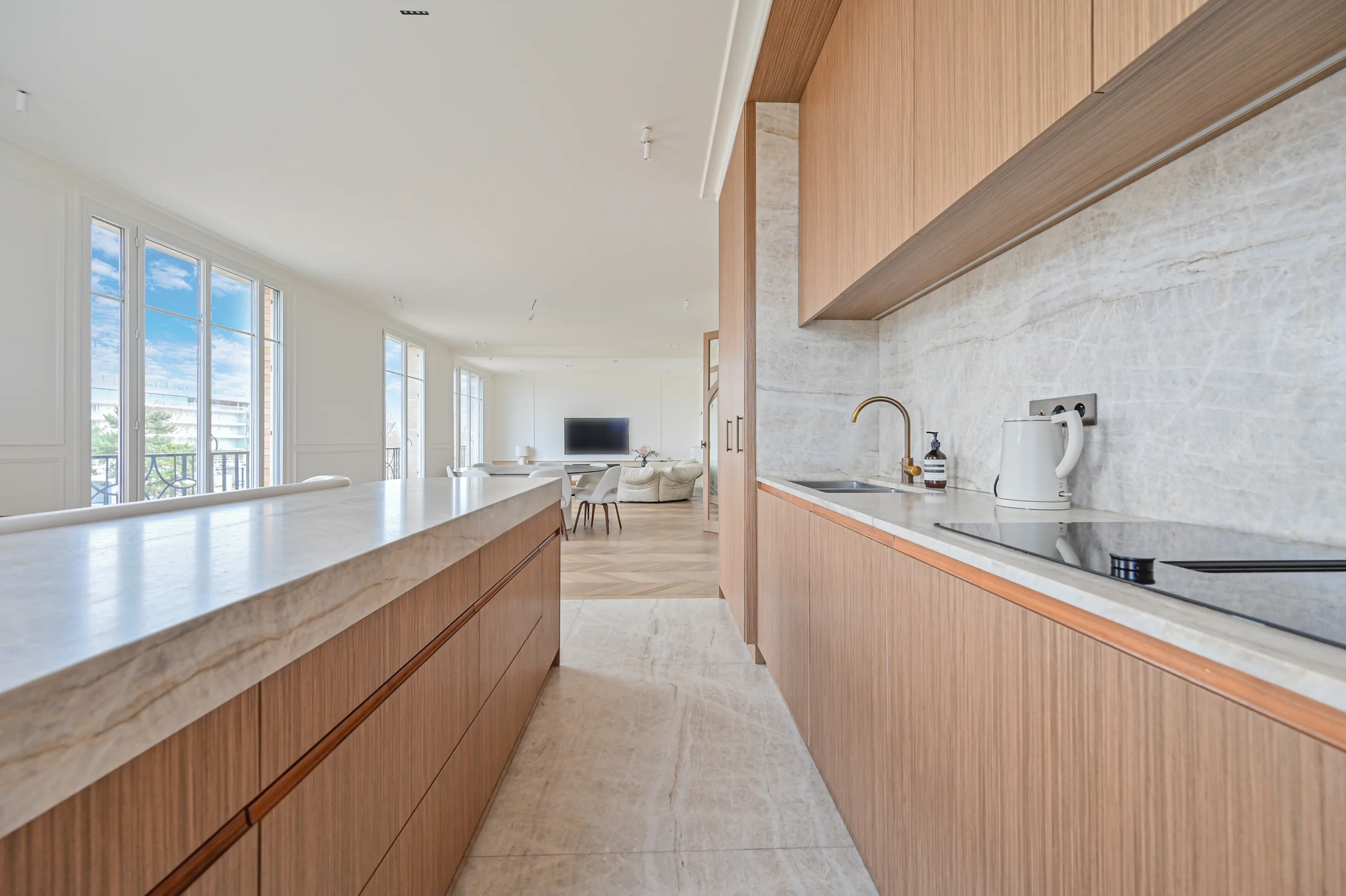 Cuisine ouverte avec îlot bois clair, plan de travail blanc et large baie vitrée donnant sur Roland-Garros