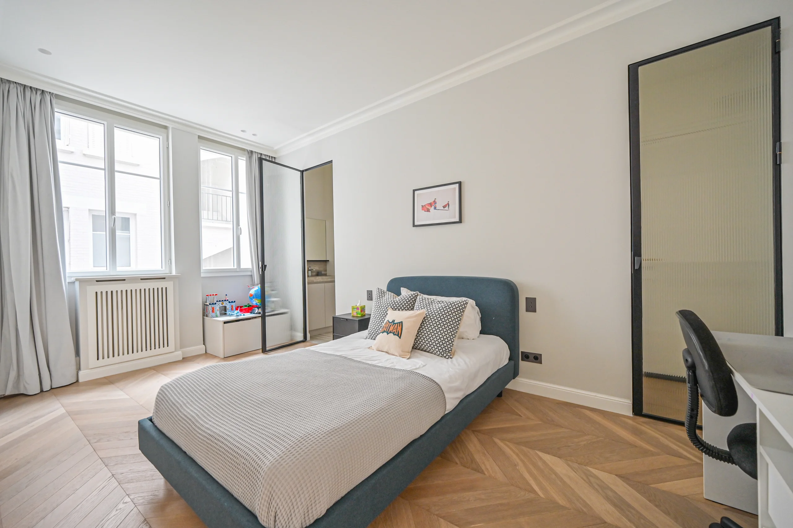 Chambre lumineuse avec lit gris, parquet chevron, baies vitrées et miroir mural encadré gris