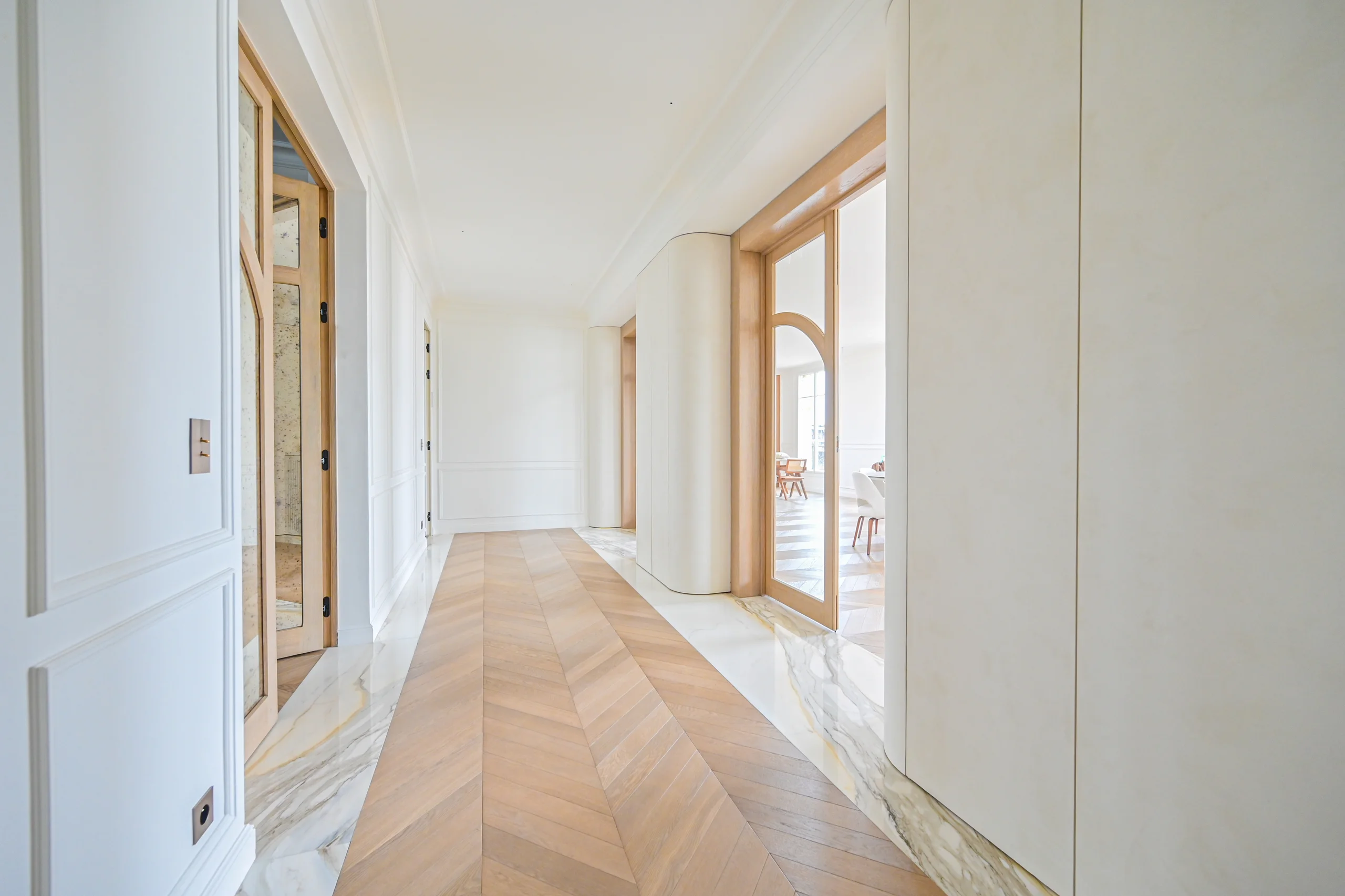Couloir lumineux aux murs blancs et portes en bois clair, sol géométrique en parquet clair, baie vitrée donnant sur terrasse