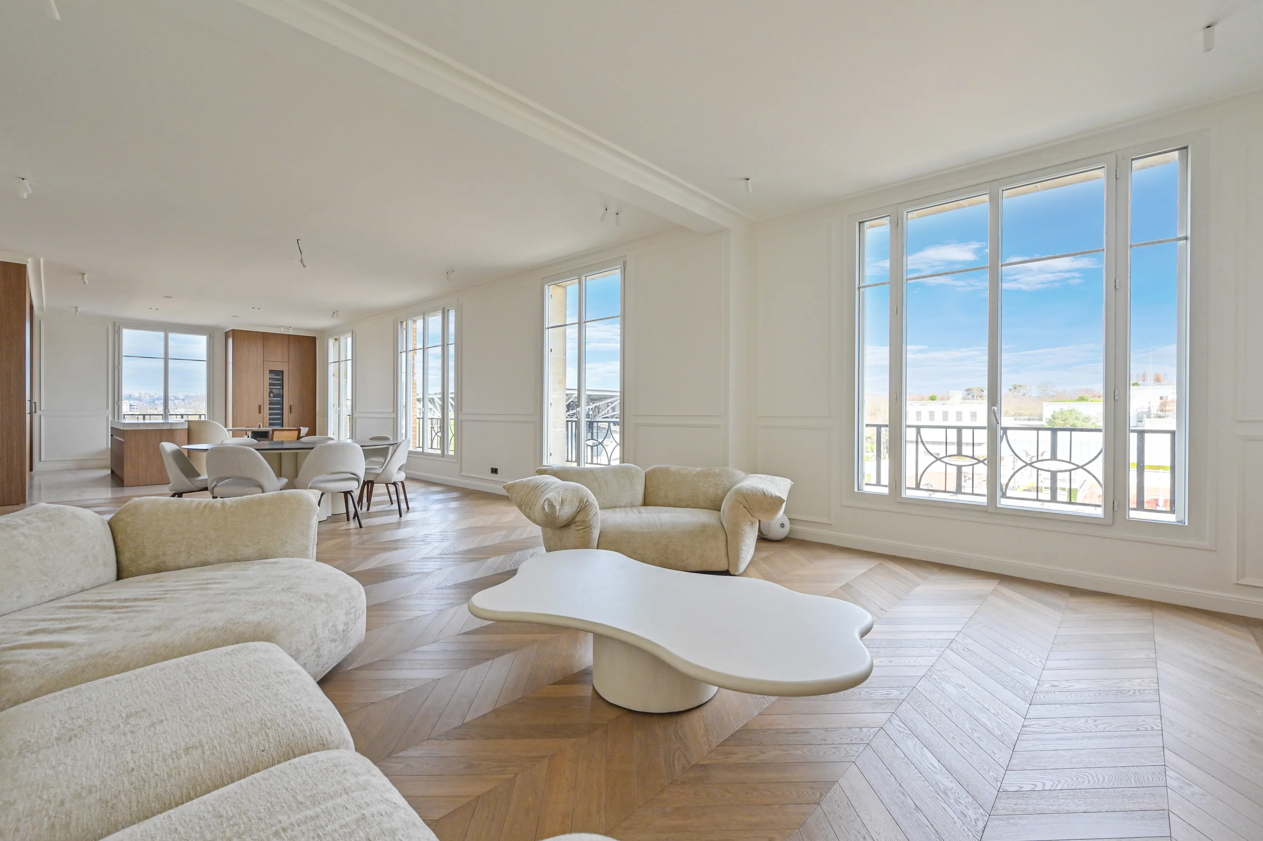 Salon spacieux aux grandes baies vitrées, parquet point de Hongrie, mobilier beige clair et table basse blanche épurée