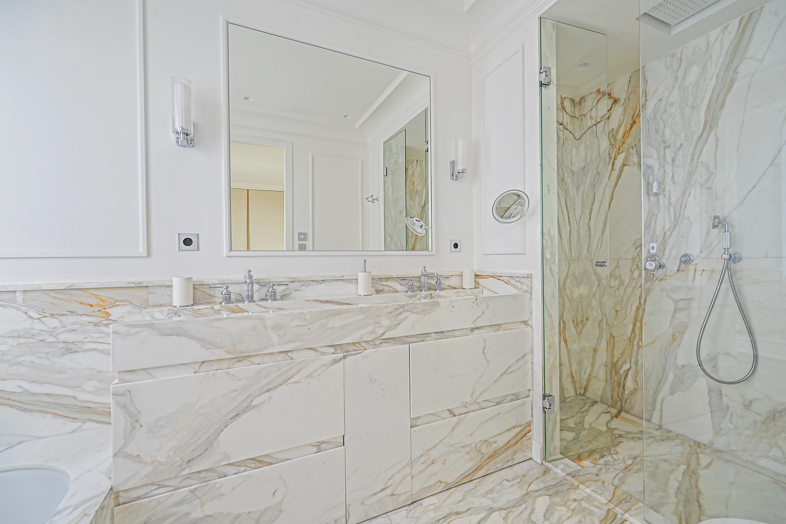 Salle de bains luxe avec marbre blanc et veines dorées, double vasque, miroir éclairé et douche italienne