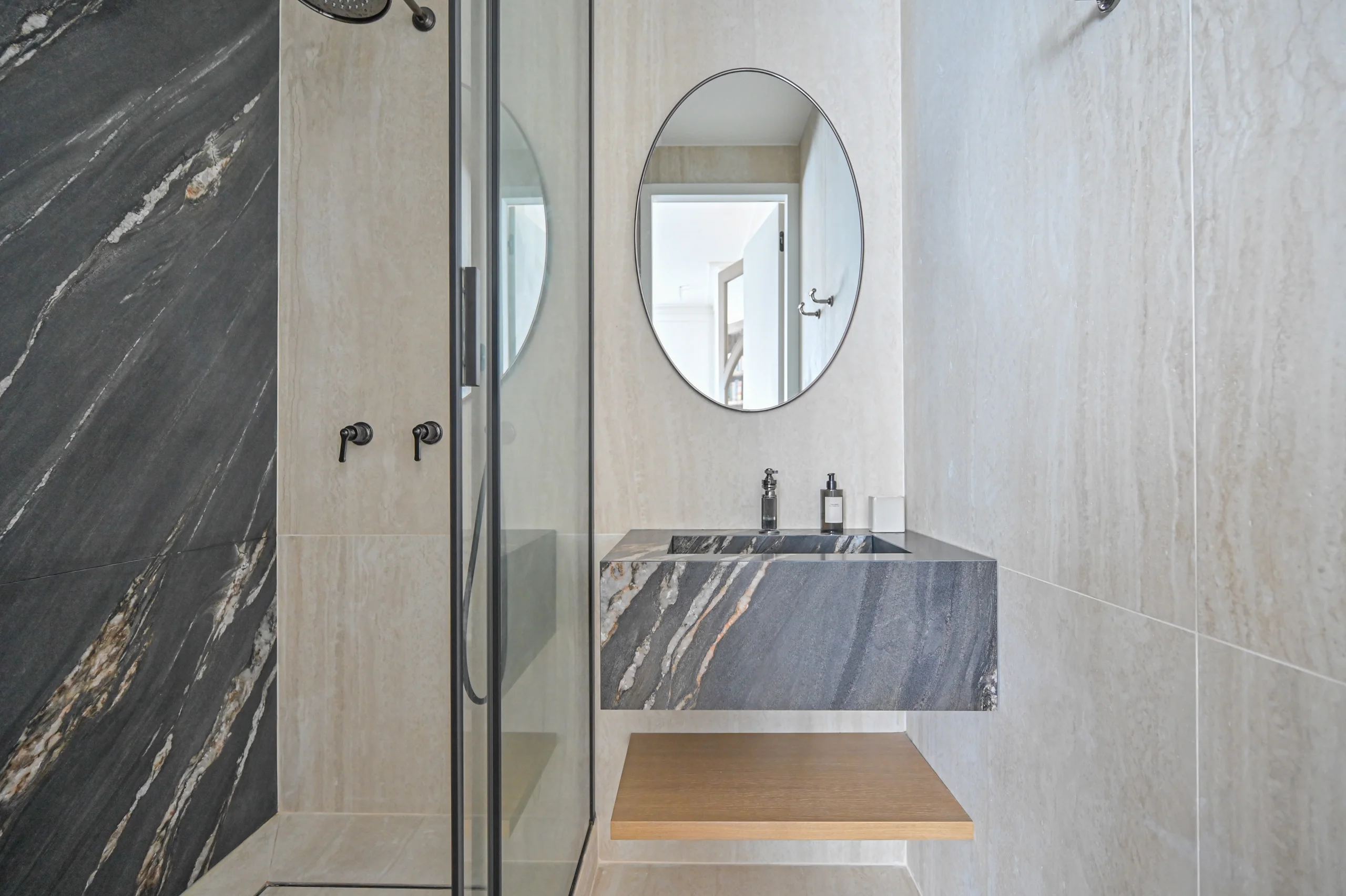 Salle de bain aux Premières Loges avec vasque en marbre gris, miroir ovale et paroi de douche vitrée