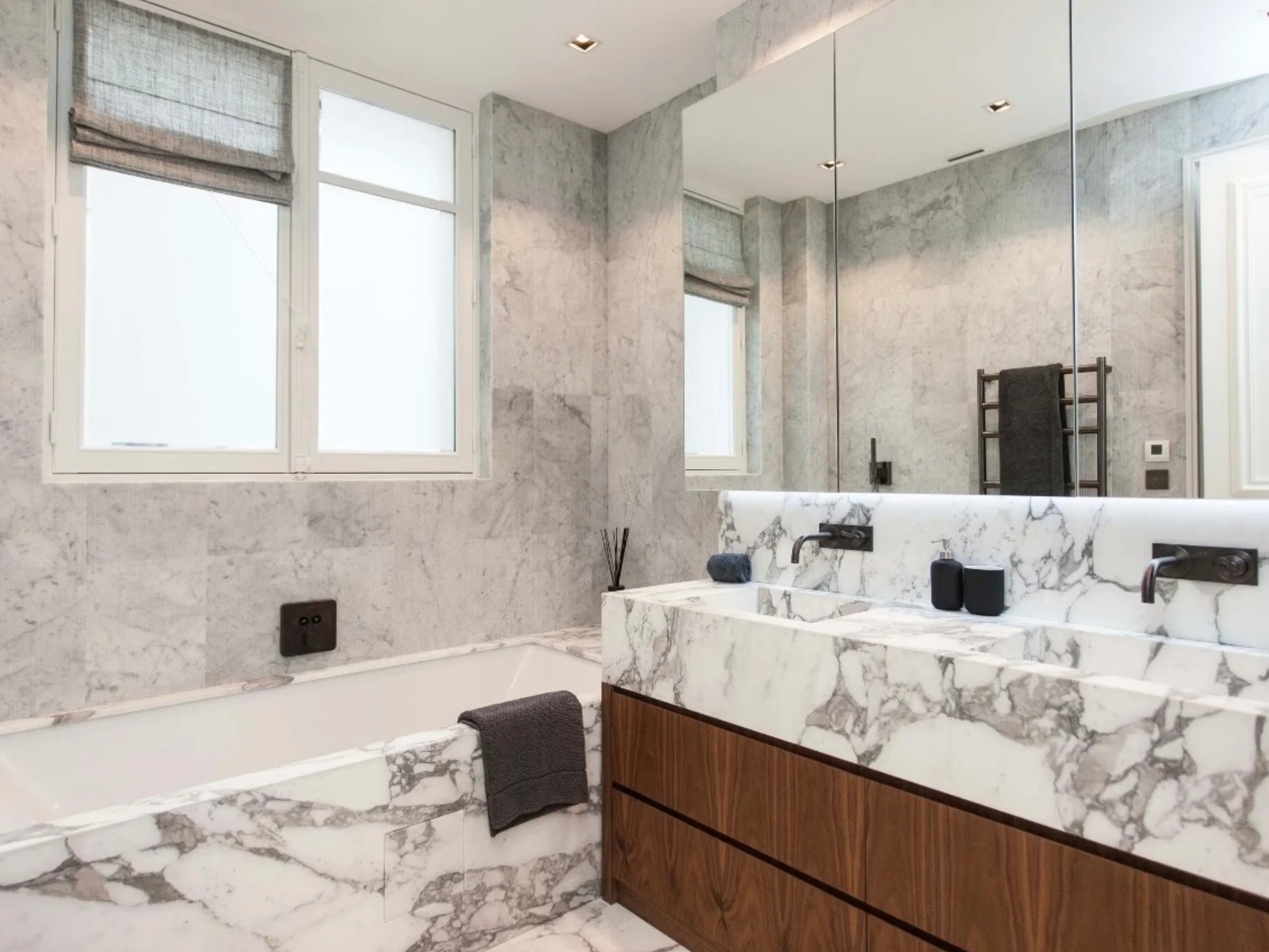 Salle de bains avec baignoire encastrée, vasques en marbre blanc, boiseries teintées et miroir antibuée, lumière naturelle