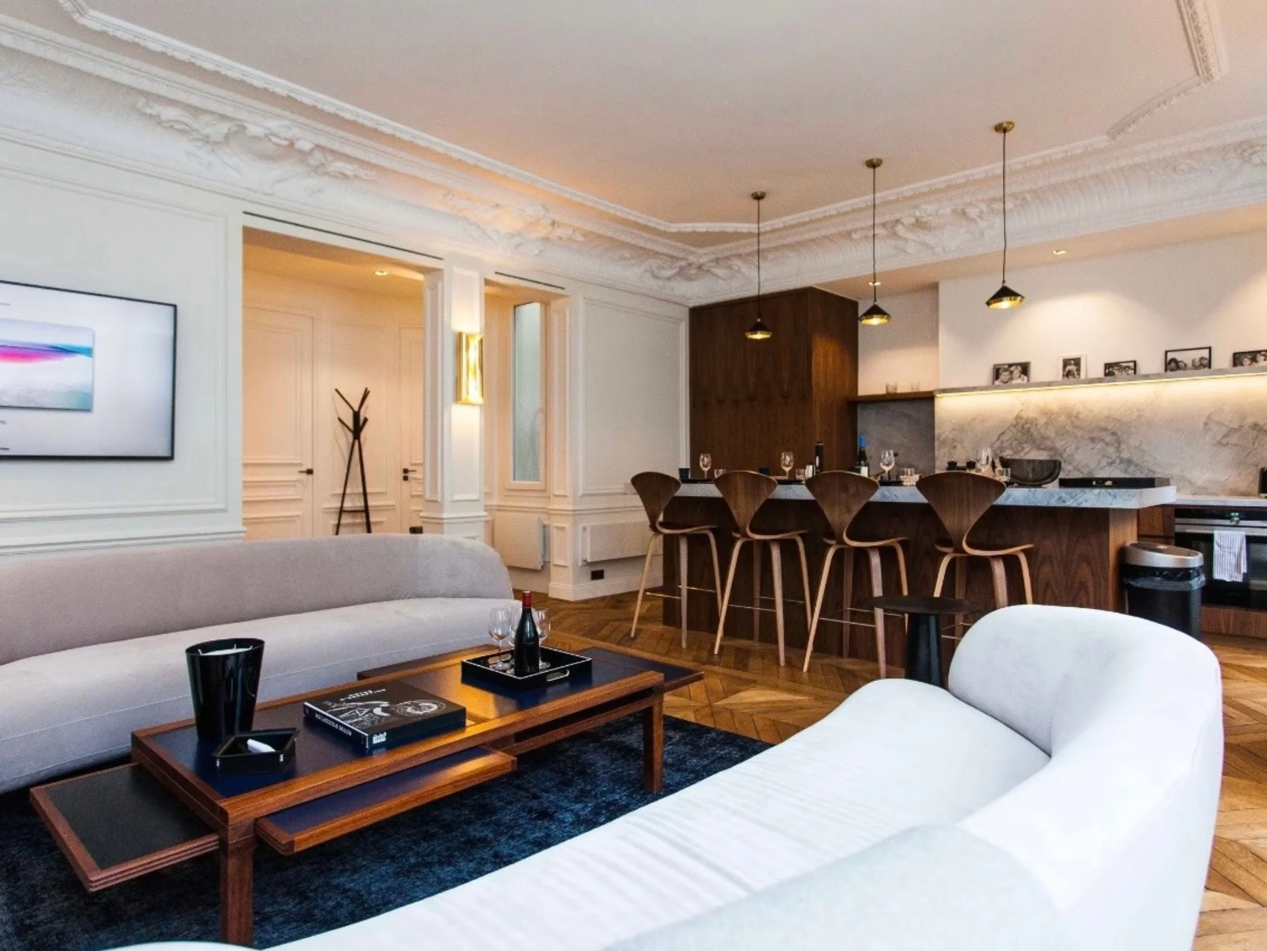 Salon moderne avec canapés blanc crème, plafond en moulures, bar en bois sombre et parquet clair